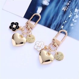 Keychains Lanyards New metal heart-shaped keychain fashionable camellia letter circular pendant womens headphone box accessory bag pavilion party gift J240509
