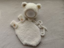 新生児の写真は、ミンクウールベアの帽子とジャンプスーツを支持します