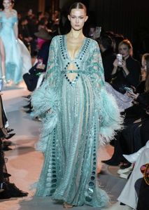 trägt ein grünes Abendkleid mit Pailletten und Federn bei der neuesten Einführung der Marke Zuhair Murad im Jahr 2023