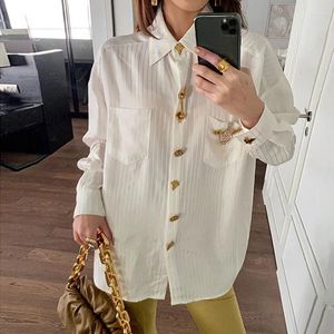 女性用ブラウスの女性ブラウスの真っ白な白い垂直ストライプシャツと金のボタンとペンダントの装飾