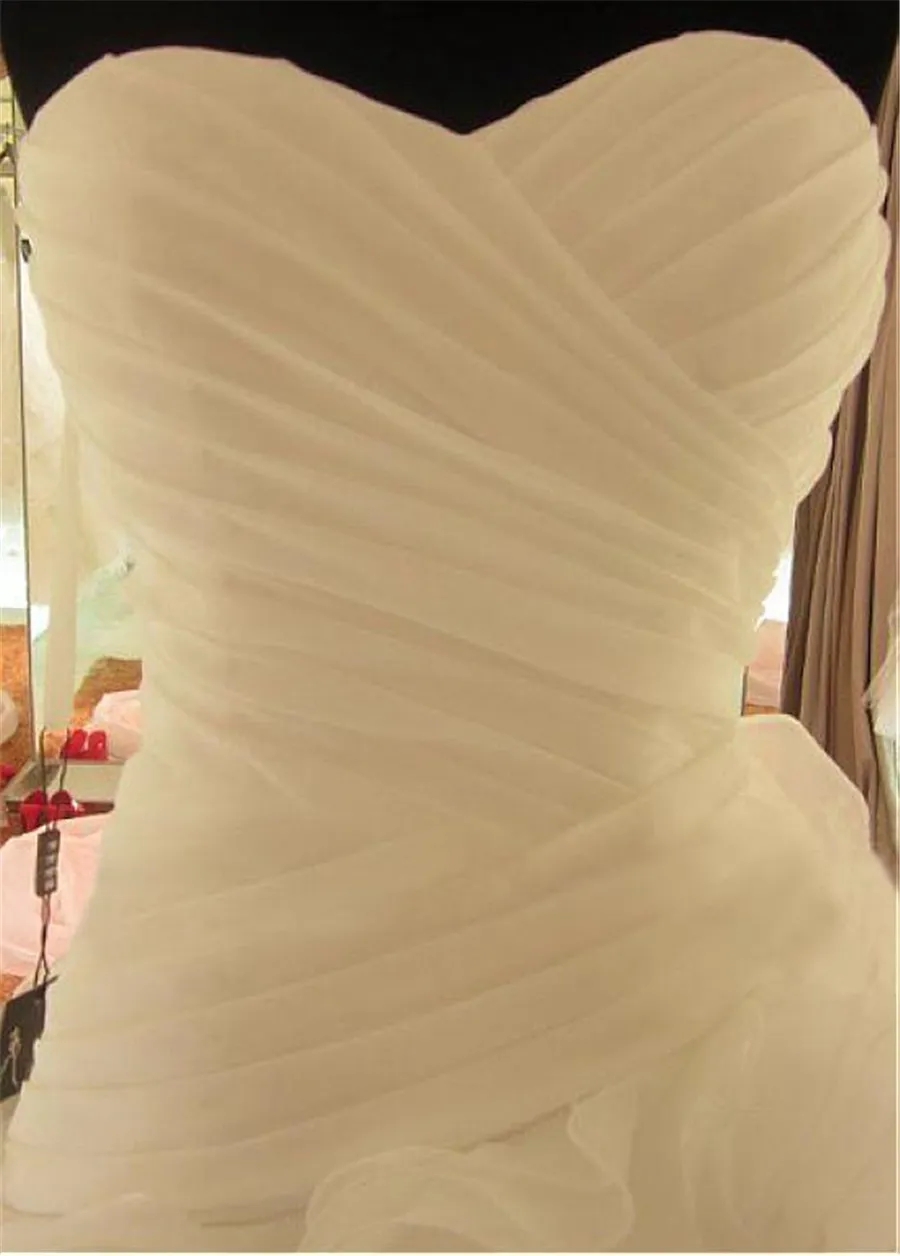 Romantisches, gerüschtes Organza-Hochzeitskleid mit herzförmigem Ausschnitt, asymmetrischer Taille und A-Linie. Hochzeitskleid von Reals mit Schnürung, versandfertig