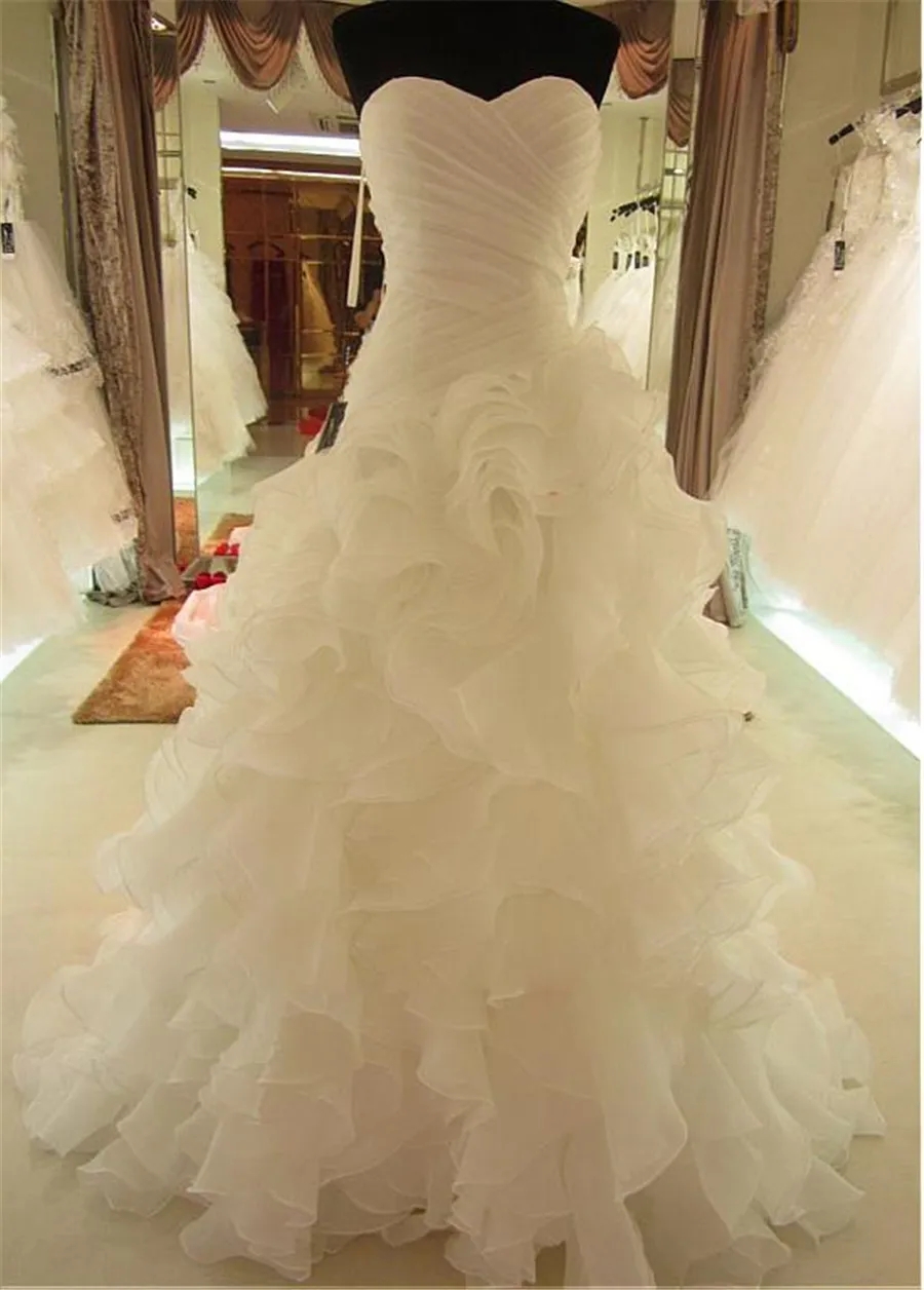 Romantisches, gerüschtes Organza-Hochzeitskleid mit herzförmigem Ausschnitt, asymmetrischer Taille und A-Linie. Hochzeitskleid von Reals mit Schnürung, versandfertig