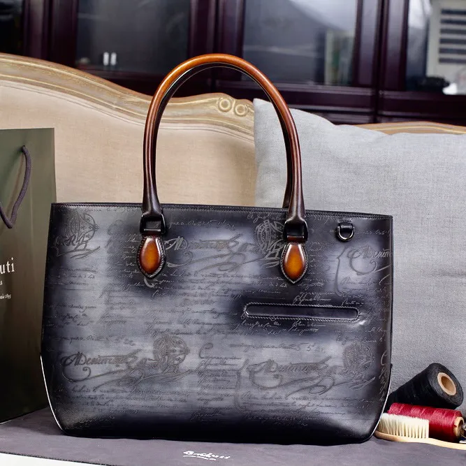 The Berluti handbag is handcrafted with antique coloring. TOUJOURS shopping bag features a large open design that can be carried on the shoulder or by hand