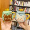 Kupalar taç kapağı ve kaşıkla seramik kupa taşıyor Süt kahve çayı suyunun çocuklar için sevimli hayvan desen fincanı
