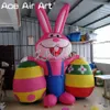8MH (26 ft) med fläkten Airbllown Easter Cartoon Rabbit rosa uppblåsbar kanin i Rompers med två påskägg för Festival Outdoor Yard -dekoration