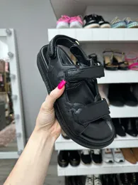 Designer 2025 skor kvinnor agerar platt sandal svart vit lammskinn krok slinga sandaler guld metall bokstav gummi enda sko två justerbara remmar